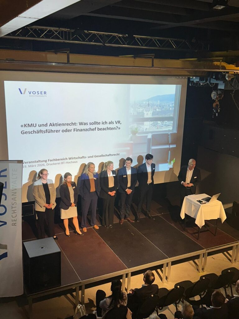 Group of professionals standing on a stage during a panel, with a large presentation screen behind them showing a German title and a city view.